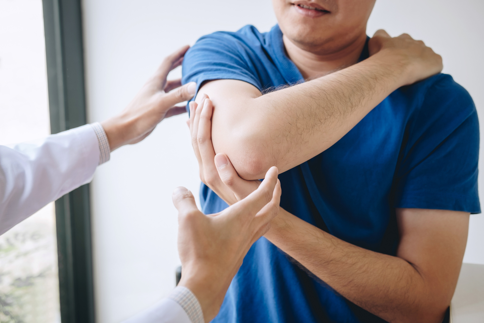 Doctor physiotherapist assisting a male patient while giving exercising treatment massaging the arm of patient in a physio room, rehabilitation physiotherapy concept
